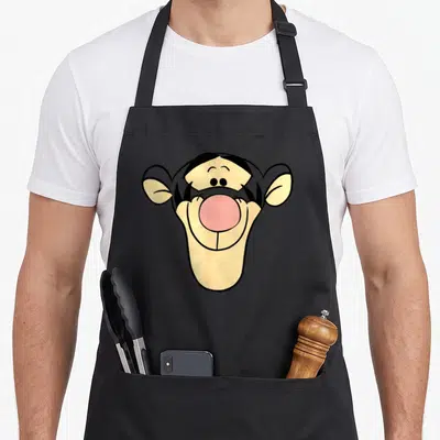 Tablier de cuisine noir avec un grand visage stylisé de Tigrou aux oreilles pointues et au nez rose.