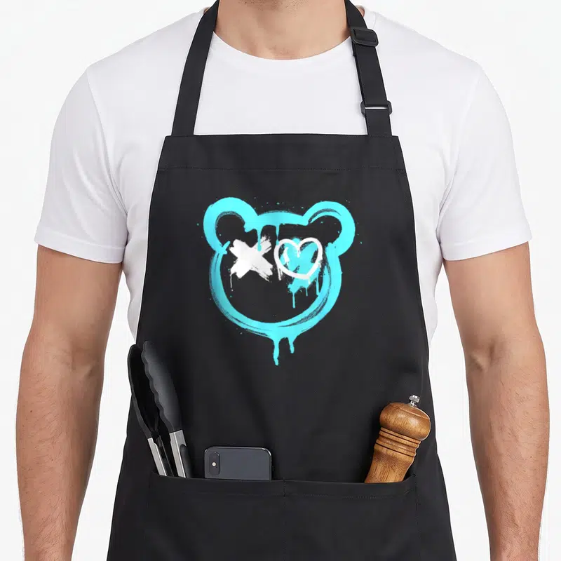 Tablier de cuisine noir avec tête d'ours stylisée en graffiti bleu cyan et motifs blancs sur le visage.