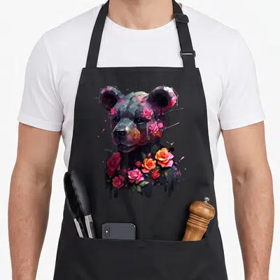 Tablier de cuisine noir avec un ours stylisé entouré de roses roses et orange.