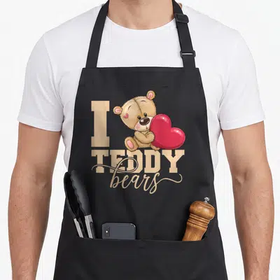 Tablier de cuisine noir avec ours en peluche beige tenant un grand cœur rose vif et du texte beige.