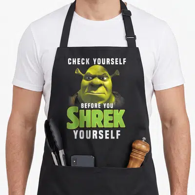 Tablier de cuisine noir avec l'illustration de Shrek et le texte Check Yourself Before You Shrek Yourself imprimé en blanc et vert.