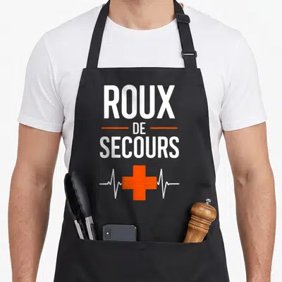 Tablier de cuisine noir avec inscription Roux de Secours et croix orange sur fond gris uni.