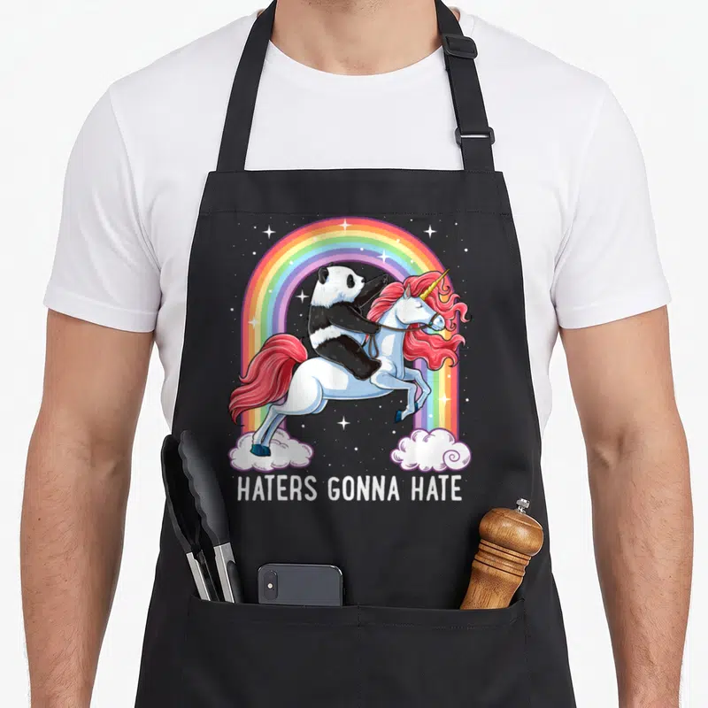 Tablier de cuisine noir avec illustration d'un panda sur une licorne rose et un arc-en-ciel coloré.
