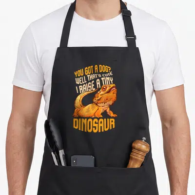 Tablier de cuisine noir avec illustration dragon barbu orange et texte « You Got A Dog Well That's Adorable I Raise A Tiny Dinosaur »