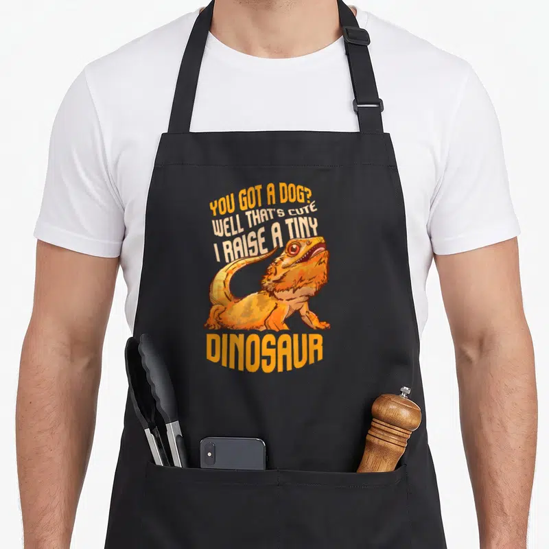 Tablier de cuisine noir avec illustration dragon barbu orange et texte « You Got A Dog Well That's Adorable I Raise A Tiny Dinosaur »
