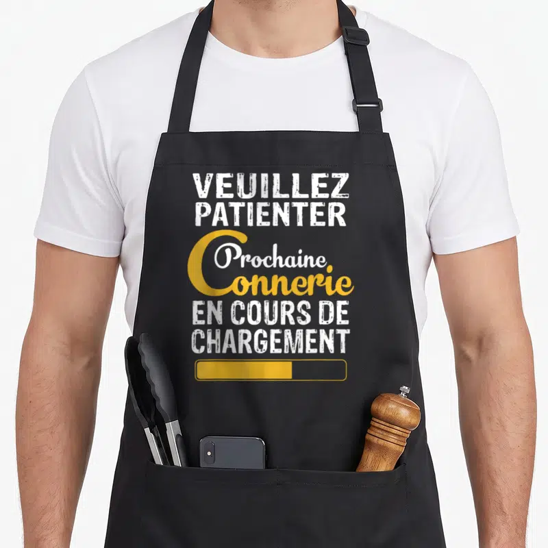 Tablier de cuisine noir avec l'inscription Veuillez Patienter Prochaine Connerie En Cours De Chargement et une barre de progression jaune.