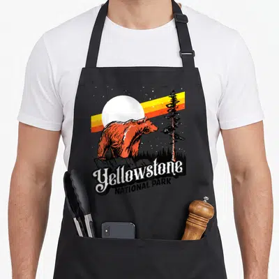 Tablier de cuisine noir avec illustration d'un ours grizzly orange devant une lune et l'inscription Yellowstone National Park.