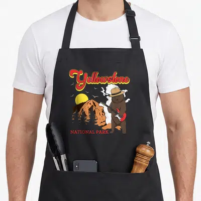 Tablier de cuisine noir avec un ours jouant de la guitare devant un volcan Yellowstone.