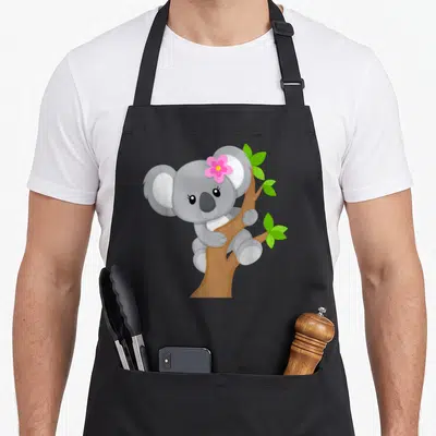 Tablier de cuisine noir avec illustration d'un koala gris portant une fleur rose sur la tête, accroché à une branche verte.
