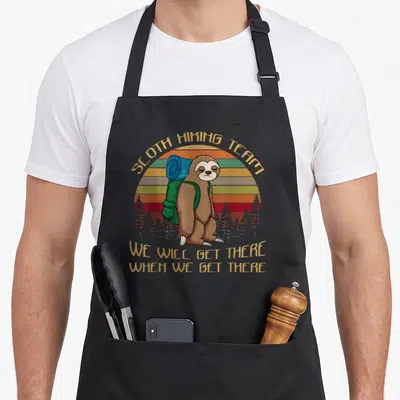 Tablier de cuisine noir avec illustration rétro d'un paresseux portant un sac à dos bleu et vert.