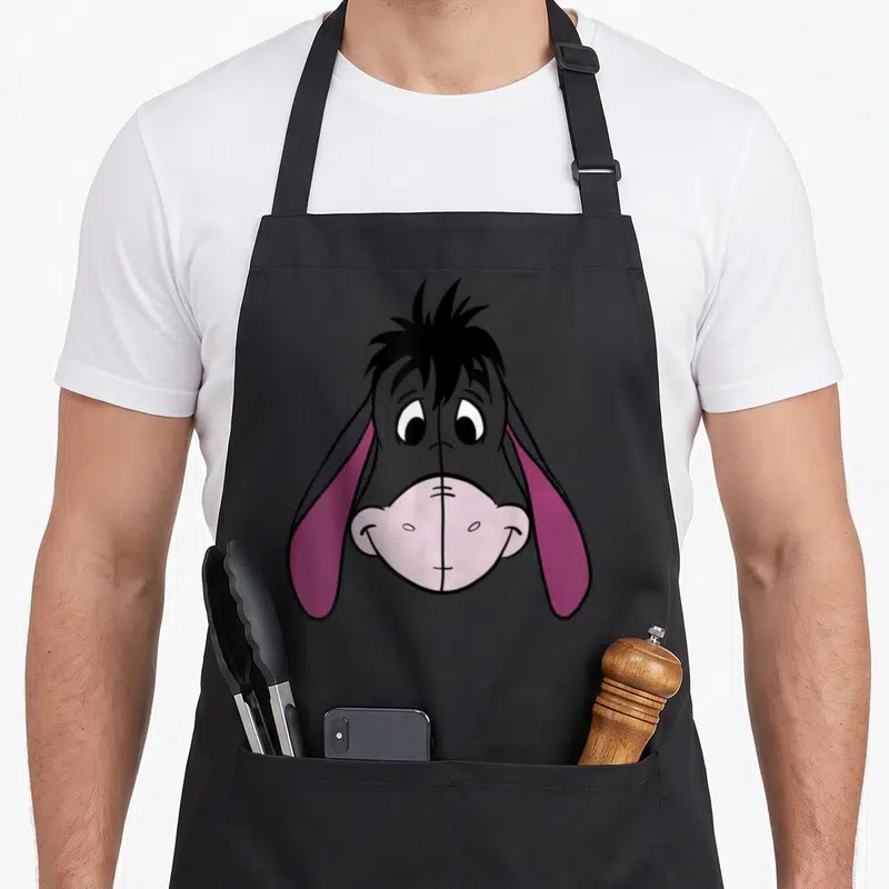 Tablier de cuisine noir avec un grand dessin coloré du visage dEeyore aux oreilles roses et au regard expressif.