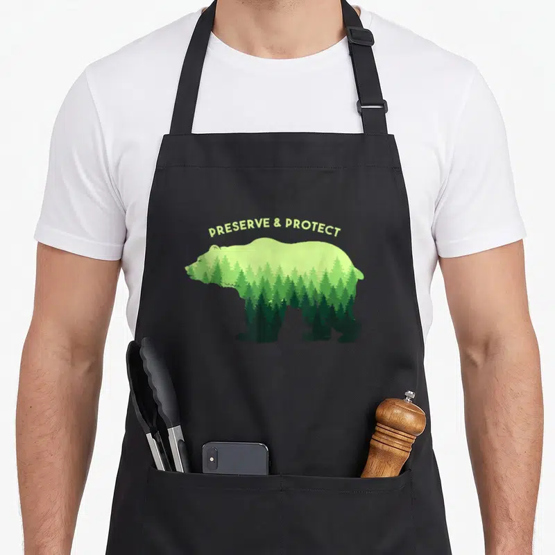 Tablier de cuisine noir avec un ours composé d'arbres verts et le texte Preserve & Protect au-dessus.