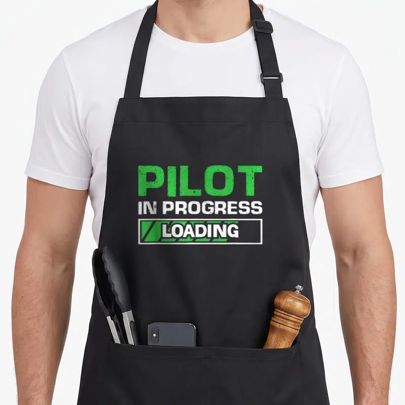Tablier de cuisine noir avec l'inscription Pilot in progress loading en vert et blanc sur le devant.