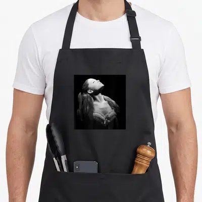 Tablier de cuisine noir avec portrait noir et blanc d'Ariana Grande regardant vers le haut et texte imprimé.