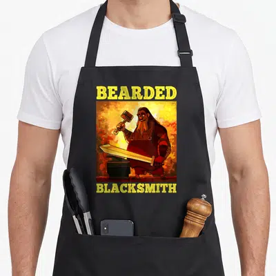 Tablier de cuisine noir avec illustration d'un forgeron barbu tenant une épée et un marteau devant un fourneau.