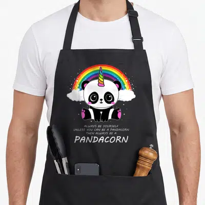 Tablier de cuisine noir avec un panda corné coloré sous un arc-en-ciel et du texte en anglais.