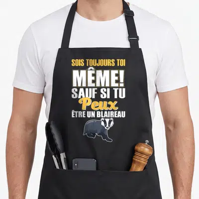 Tablier de cuisine noir avec texte jaune et blanc et illustration d'un blaireau gris en bas du motif imprimé.