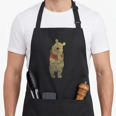 Tablier de cuisine noir avec Winnie l'ourson portrait simple au col en V rouge, style illustration vintage texturée.