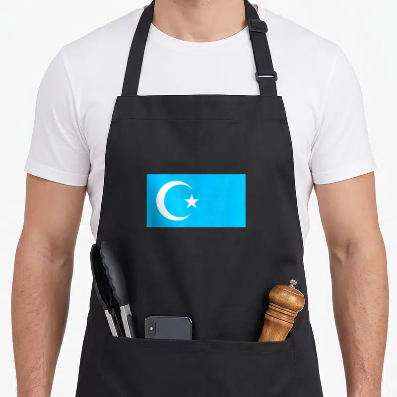 Tablier de cuisine noir avec un rectangle bleu portant un croissant et une étoile blancs.