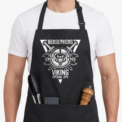 Tablier de cuisine noir avec un ours viking berserker en logo blanc, haches croisées et texte viking special ops.