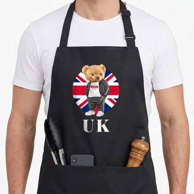 Tablier de cuisine noir avec ours britannique en survêtement devant un drapeau Union Jack circulaire et l'inscription UK.