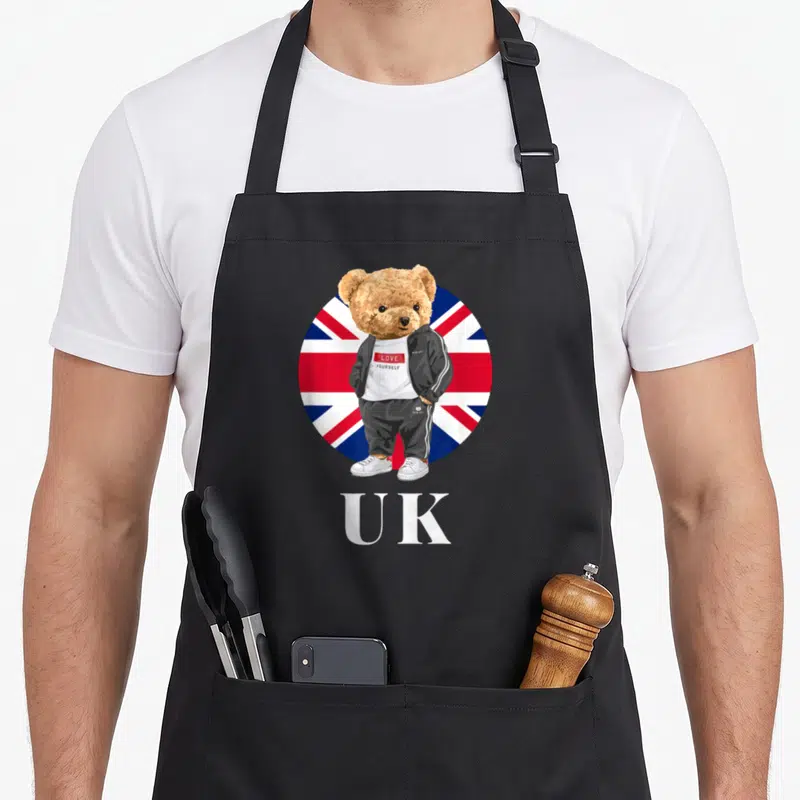 Tablier de cuisine noir avec ours britannique en survêtement devant un drapeau Union Jack circulaire et l'inscription UK.