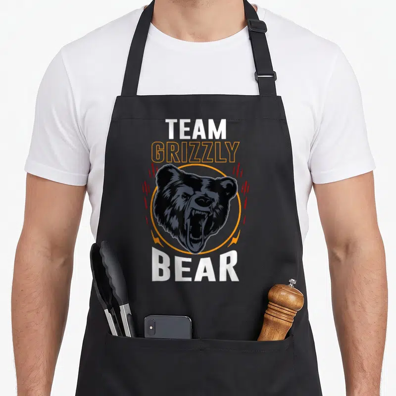Tablier de cuisine noir avec tête d'ours grizzley féroce et texte Team Grizzly Bear imprimé en blanc et orange.