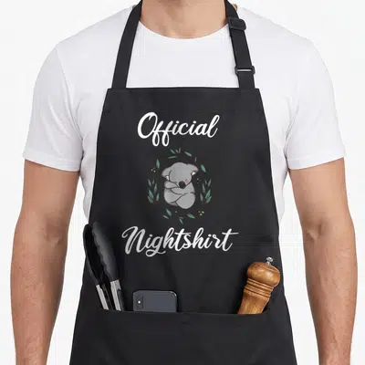 Tablier de cuisine noir avec un koala gris dormant et le texte Official Nightshirt en blanc.