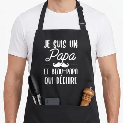 Tablier de cuisine noir avec inscription blanche Je suis un Papa et beau-papa qui déchire surmonté d'une moustache stylisée.