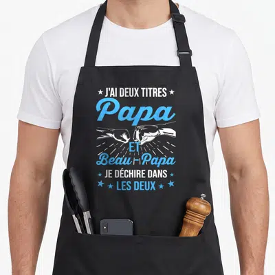 Tablier de cuisine noir avec texte blanc et bleu J'ai deux titres Papa et Beau-Papa et illustration de poings s'écrasant.