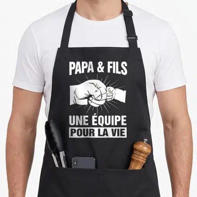 Tablier de cuisine noir avec l'inscription Papa et Fils Une équipe pour la vie au-dessus d'un poing de papa et d'un poing d'enfant.