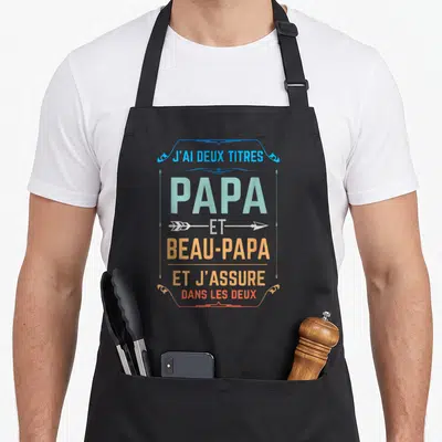 Tablier de cuisine noir avec inscription typographique colorée J'ai deux titres Papa et Beau-papa et j'assure dans les deux.