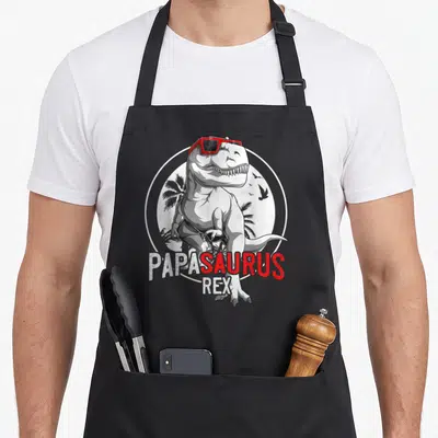 Tablier de cuisine noir avec dinosaure Tyrannosaurus Rex portant des lunettes de soleil rouges et le texte Papa Saurus Rex.