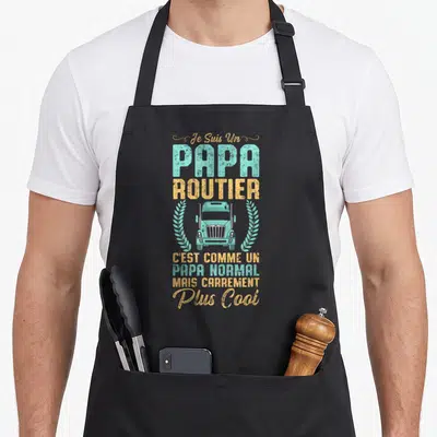 Tablier de cuisine noir avec texte Je Suis Un Papa Routier et illustration de truck turquoise encadré de branches dorées.