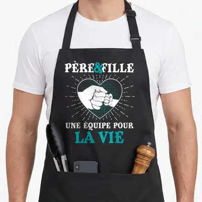 Tablier de cuisine noir avec illustration d'un poing pressé dans un cœur et texte blanc et turquoise.