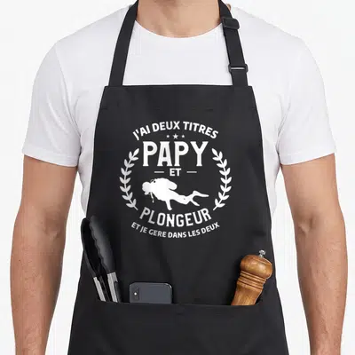 Tablier de cuisine noir avec inscription blanche J'ai deux titres Papy et plongeur et une silhouette de plongeur encadrée par des branches.