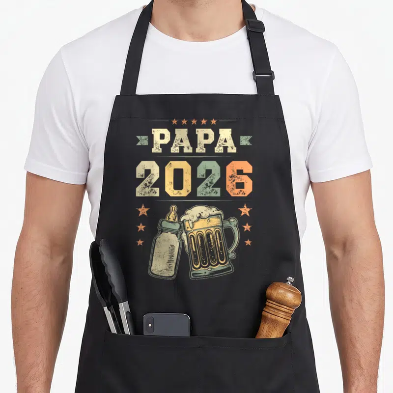 Tablier de cuisine noir avec inscription Papa 2026, illustration biberon et bière vintage aux couleurs pastel.