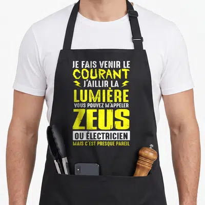 Tablier de cuisine noir avec texte jaune et blanc citant Zeus et l'électricien pour une fête des pères humoristique.