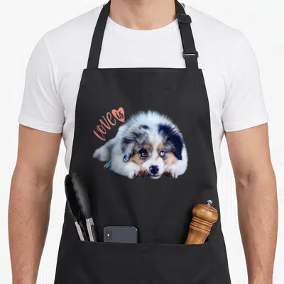 Tablier de cuisine noir avec un chiot berger australien et le texte Love Is Dog en rose.