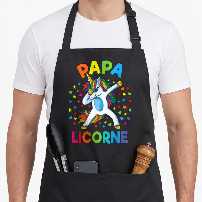 Tablier de cuisine noir avec licorne blanche en position dab, mane arc-en-ciel et texte Papa Licorne coloré.