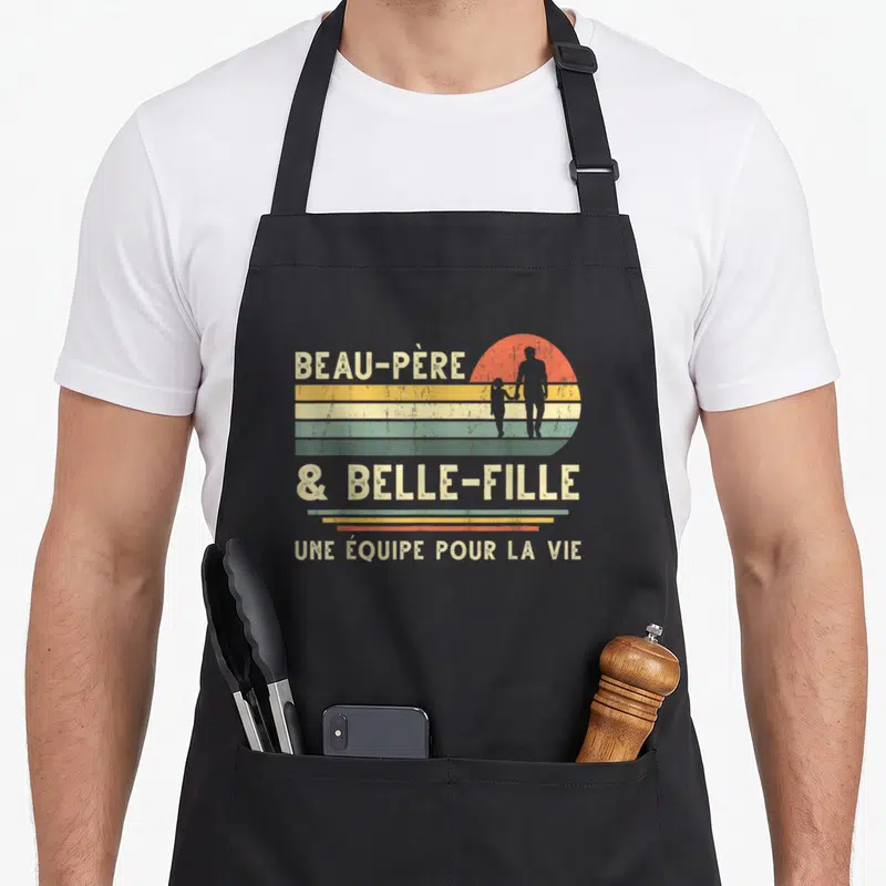 Tablier de cuisine noir avec illustration vintage d'un adulte tenant la main d'un enfant devant un soleil couchant coloré.