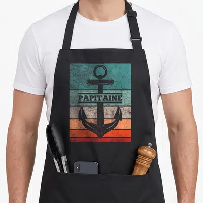 Tablier de cuisine noir avec ancre grise sur bandes colorées et l'inscription Papitaine en style rétro.