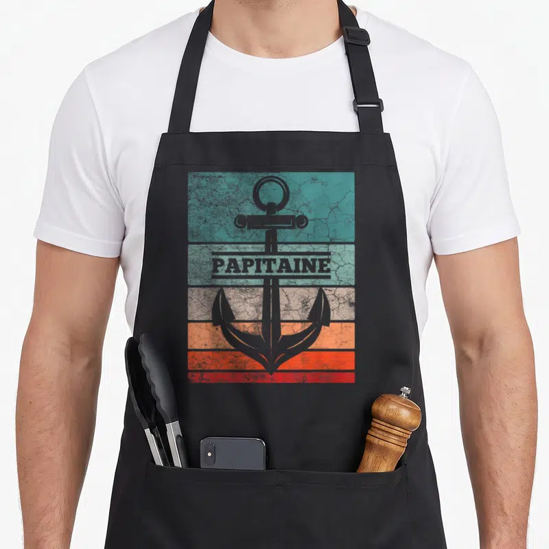 Tablier de cuisine noir avec ancre grise sur bandes colorées et l'inscription Papitaine en style rétro.
