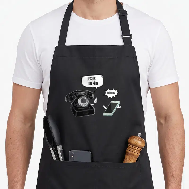 Tablier de cuisine noir avec téléphone rotatif criant je suis ton père face à un smartphone effrayé.
