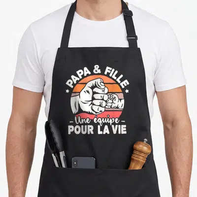 Tablier de cuisine noir avec une illustration de poings et le texte Papa et Fille une équipe pour la vie en blanc.