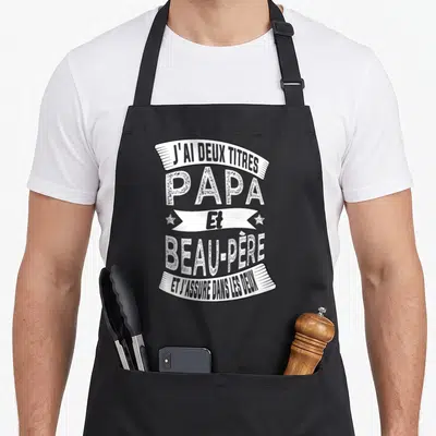 Tablier de cuisine noir avec inscription blanche J'ai deux titres Papa et beau-père et j'assure dans les deux sur banderoles.