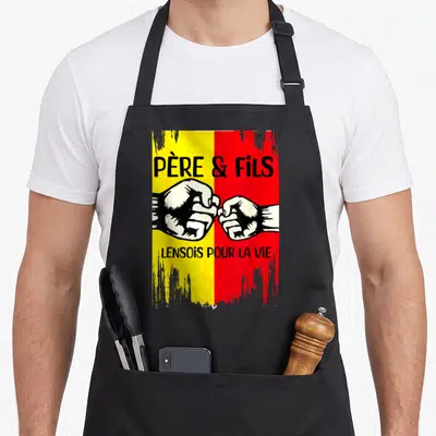 Tablier de cuisine noir avec deux poings se touchant sur un fond jaune et rouge texturé.
