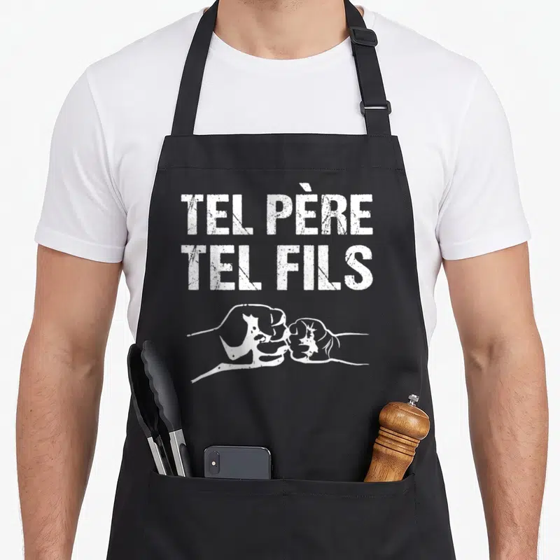 Tablier de cuisine noir avec inscription Tel Père Tel Fils et illustration de deux poings qui se touchent en blanc.