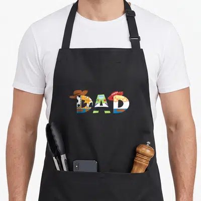 Tablier de cuisine noir avec le mot Dad composé des personnages Woody Buzz Lightyear et Jessie en couleurs vives.