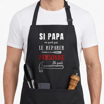 Tablier de cuisine noir avec texte blanc et rouge et illustrations d'un tournevis et d'un marteau.